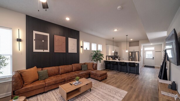A modern living room with a sectional sofa, a coffee table, and a dining area with a kitchen in the background. - Game Room! Modern 3BR 2.5BA New Build Luxury—Near Downtown Cleveland! (Cleveland)