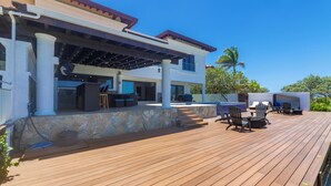 Une terrasse en bois avec des sièges extérieurs, un espace couvert et un mur en pierre.