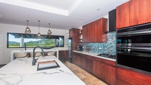 Une cuisine moderne dotée d’un plan de travail en marbre, de meubles en bois, d’une cuisinière encastrée et de luminaires suspendus.