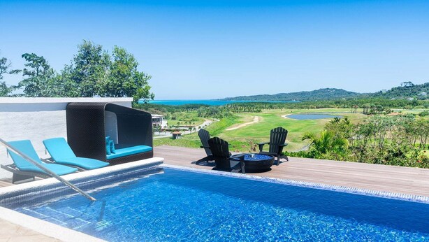 Une piscine dotée de chaises longues et d’un jacuzzi, offrant une vue sur un terrain de golf et des collines.