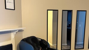 A massage chair in a room with a fireplace, a mirror, and a framed 'home' sign on the wall. - North Hills/Gym/Sauna/Massage Chair/Pool (Raleigh)