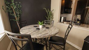 A round dining table with six chairs, a potted plant, and a kitchen area with a sink and cabinets. - North Hills/Gym/Sauna/Massage Chair/Pool (Raleigh)