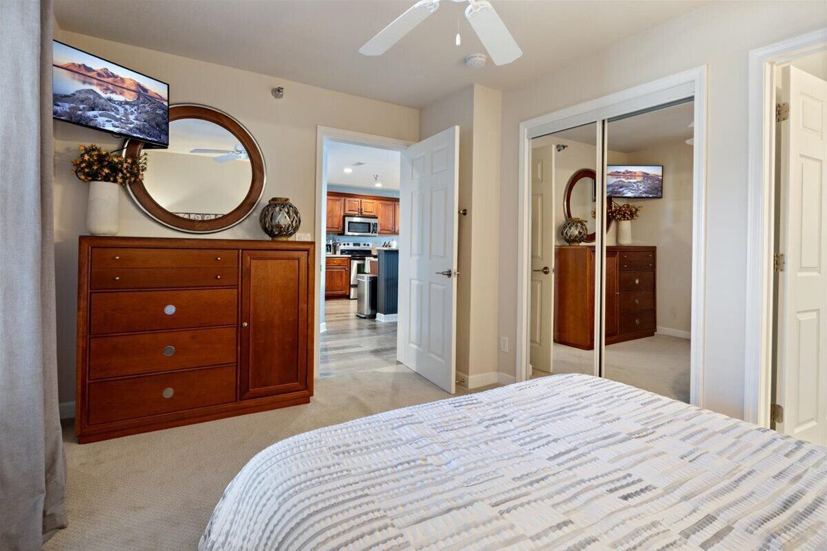 Een slaapkamer met een groot bed, een houten dressoir en een televisie boven een spiegel.
