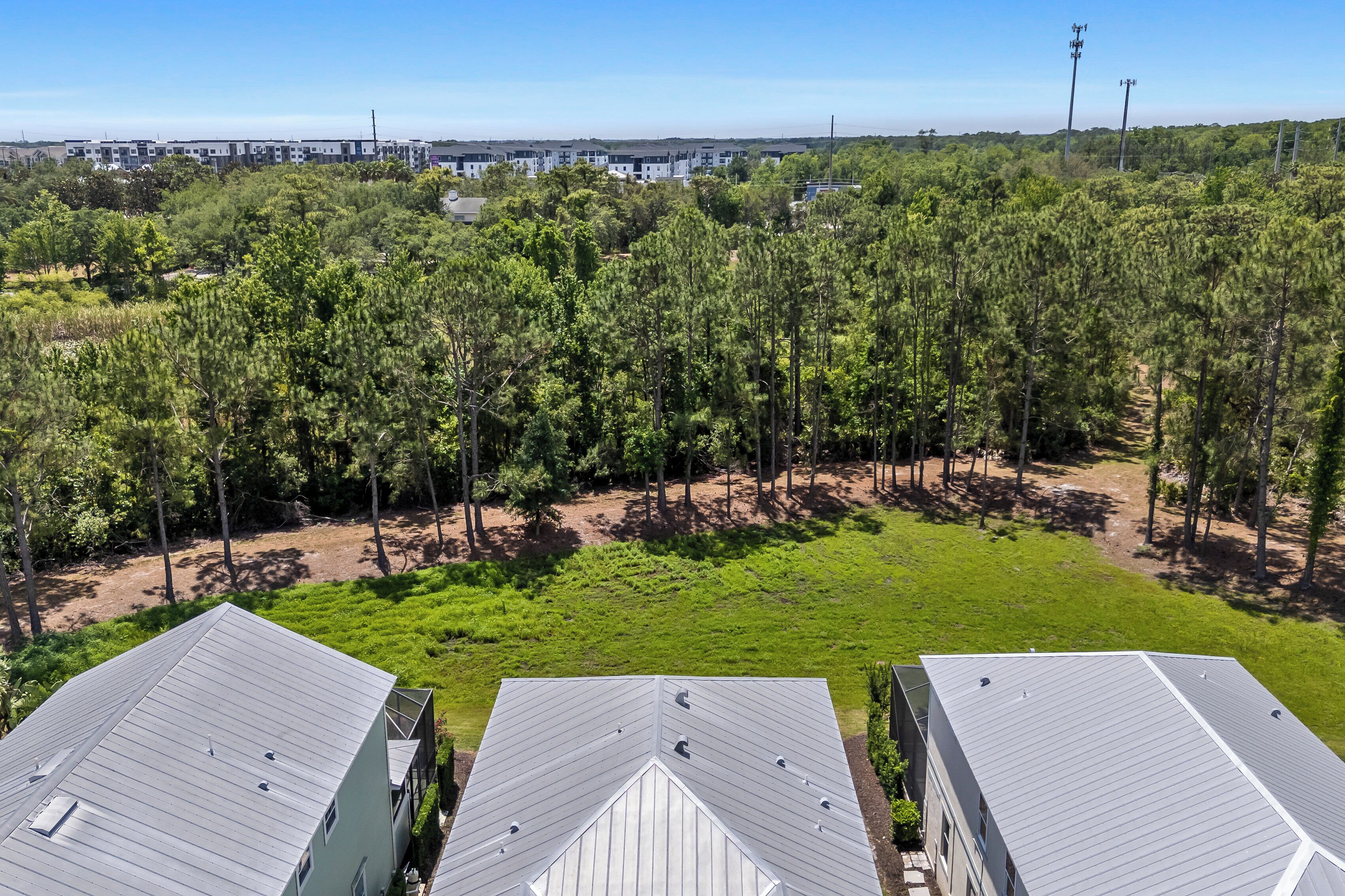 A residential area with multiple houses, a grassy field, and a dense forest in the background.