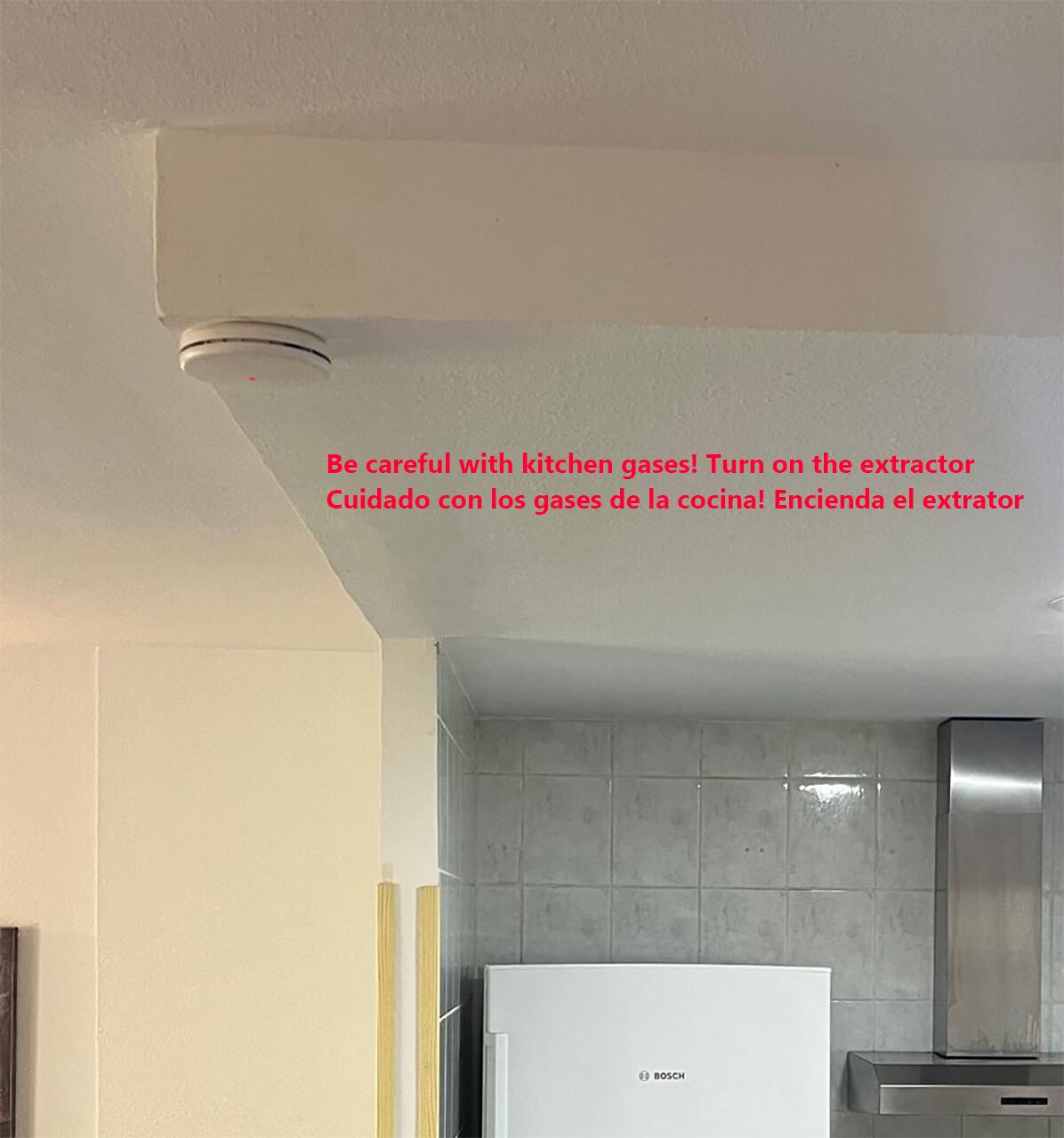 Een keuken met een Bosch koelkast, een grijze betegelde achterwand en een roestvrijstalen afzuigkap.