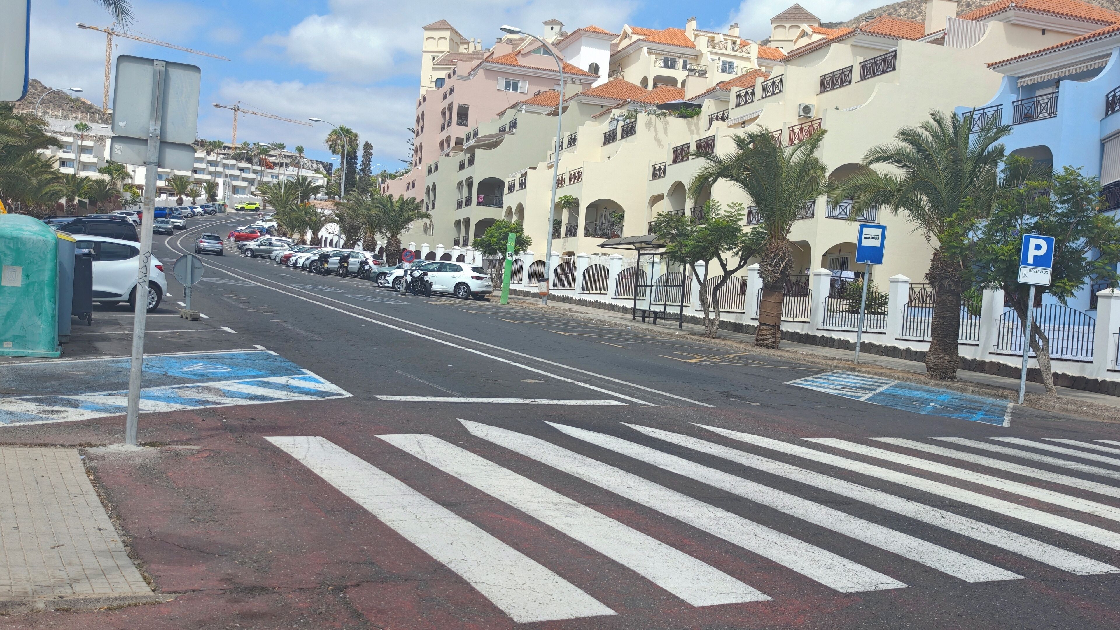 A street view with a pedestrian crossing, parked cars, and a building with balconies.