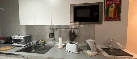 Una cocina moderna con armarios blancos, un lavamanos de acero inoxidable, un microondas, un tostador y una cafetera.