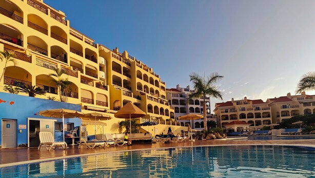 A hotel with a swimming pool, multiple balconies, and outdoor seating areas.