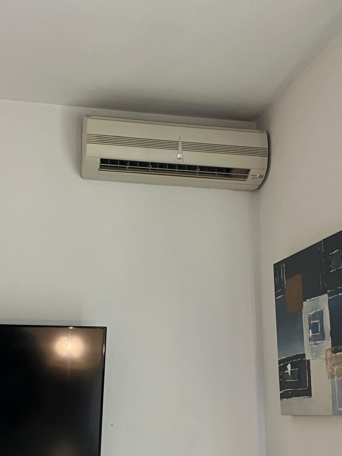 A room with a mounted air conditioner, a flat-screen TV, and a painting on the wall.