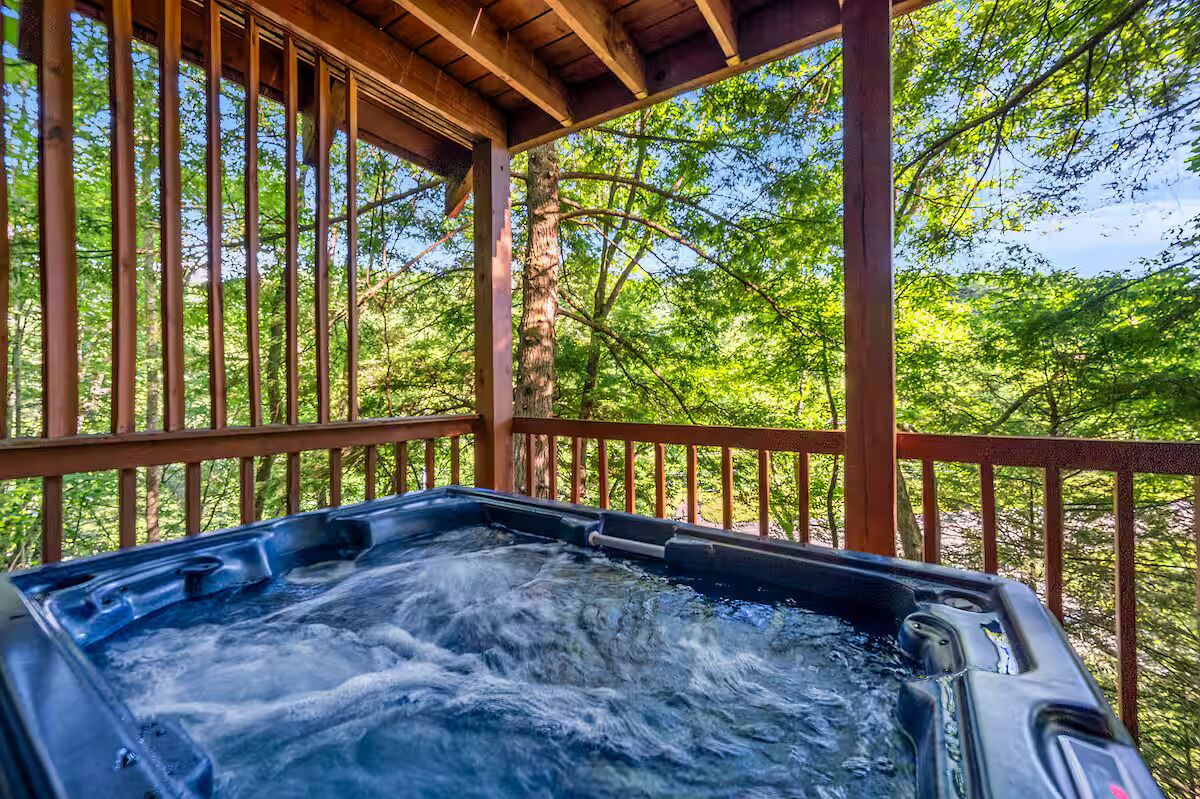 A hot tub under a wooden pergola with a view of a forested area.