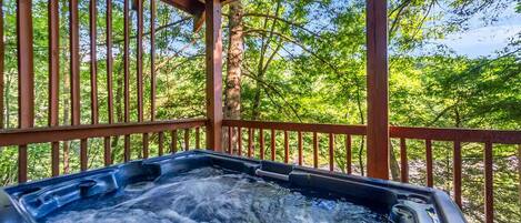 A hot tub under a wooden pergola with a view of a forested area.