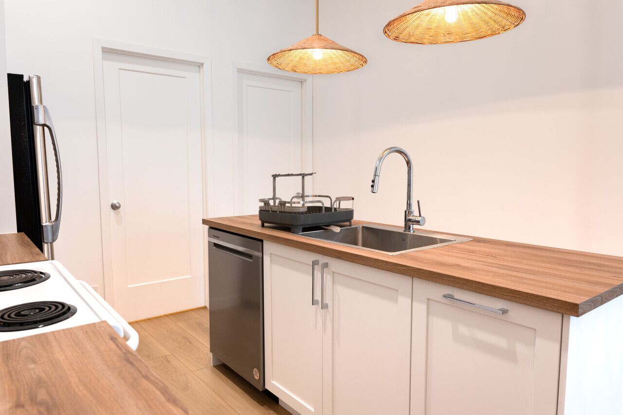 A modern kitchen with a stove, dishwasher, sink, and two wicker pendant lights.