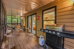 Eine überdachte Veranda mit Grill, Gasflasche und Essbereich mit Stühlen und Tisch.