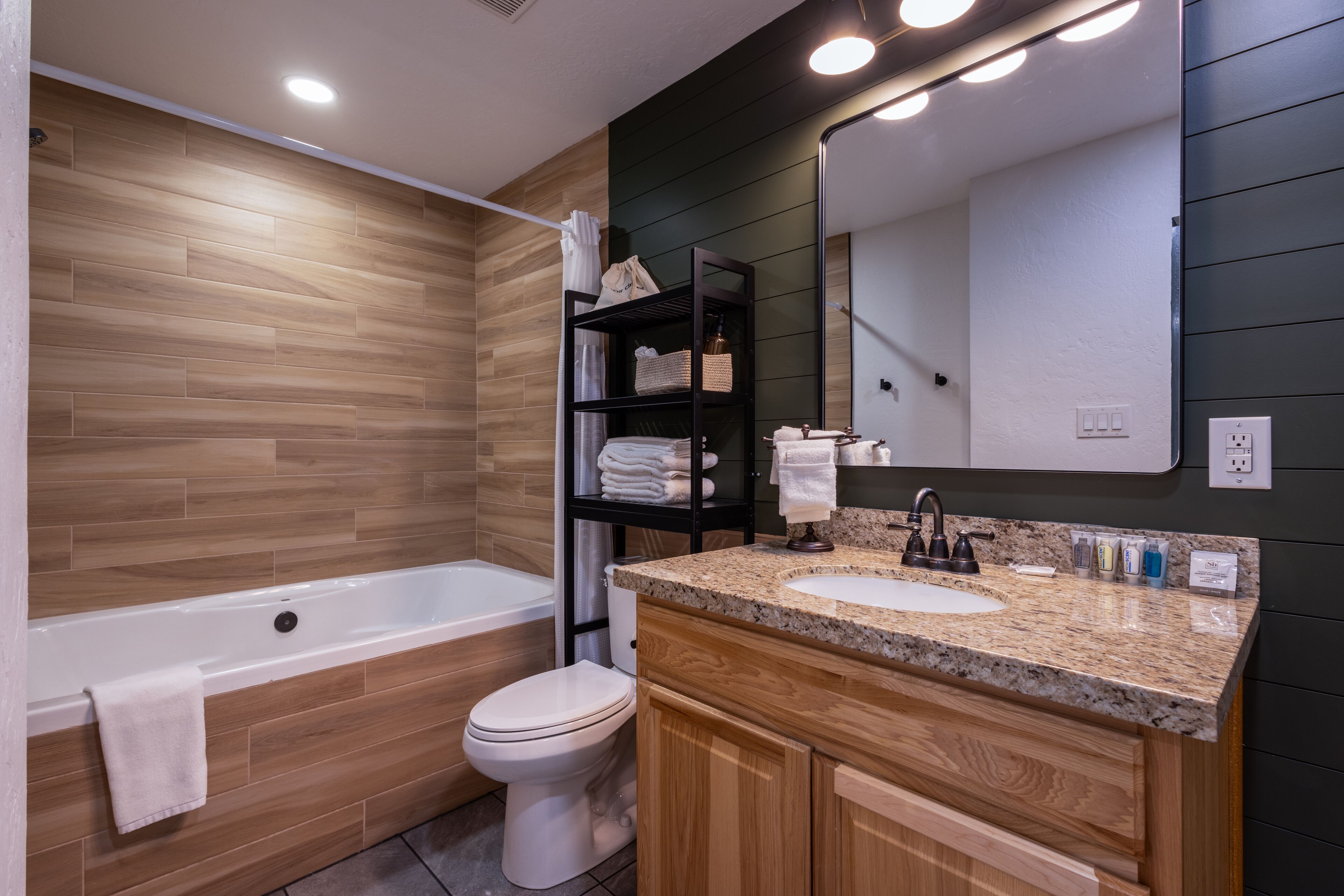A modern bathroom with a wooden vanity, a bathtub, and a toilet.