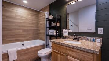 A modern bathroom with a wooden vanity, a bathtub, and a toilet.