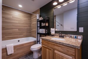A modern bathroom with a wooden vanity, a bathtub, and a toilet.