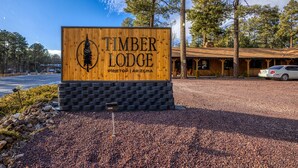 A wooden sign for Timber Lodge in Pine Top, Arizona, with a gravel driveway and a building in the background. - Timber Lodge (Pinetop-Lakeside)