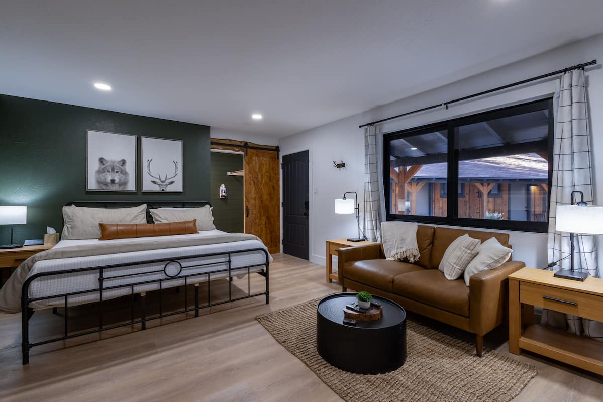 A bedroom with a bed, a brown leather sofa, a round coffee table, and a window with curtains.