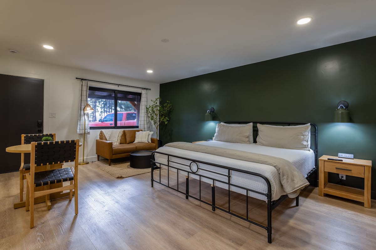 A bedroom with a bed, bedside table, and a window with a view of a red car outside.