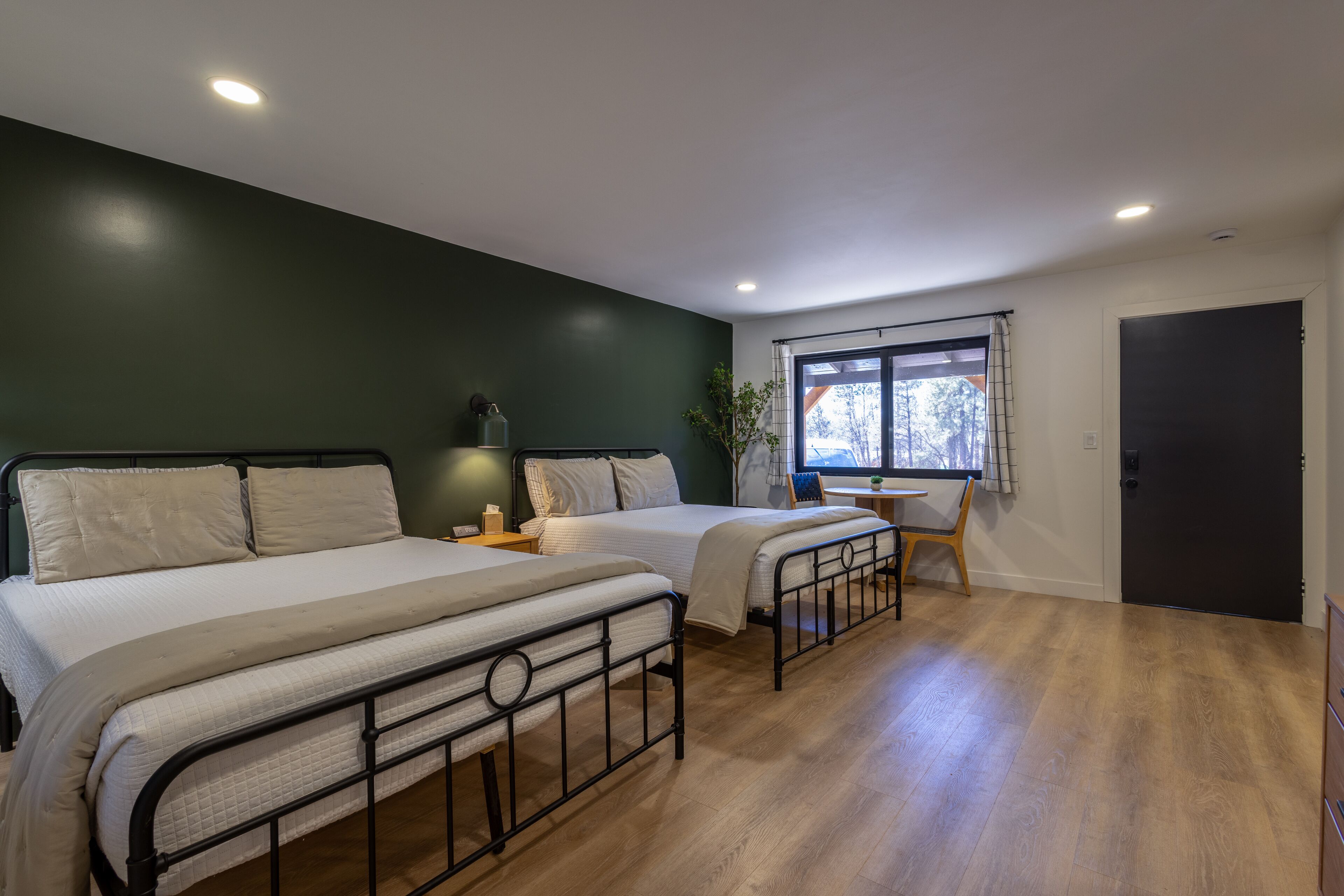 A bedroom with two beds, a desk, a chair, a window with a view, and a door.