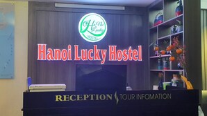 A reception desk with a neon sign for Hanoi Lucky Hostel, a map, and a shelf with decorative items. - Hanoi Lucky Hotel (Hanoi)