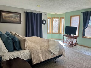 Une chambre à coucher avec un lit, un téléviseur posé sur un meuble et une fenêtre avec des rideaux.