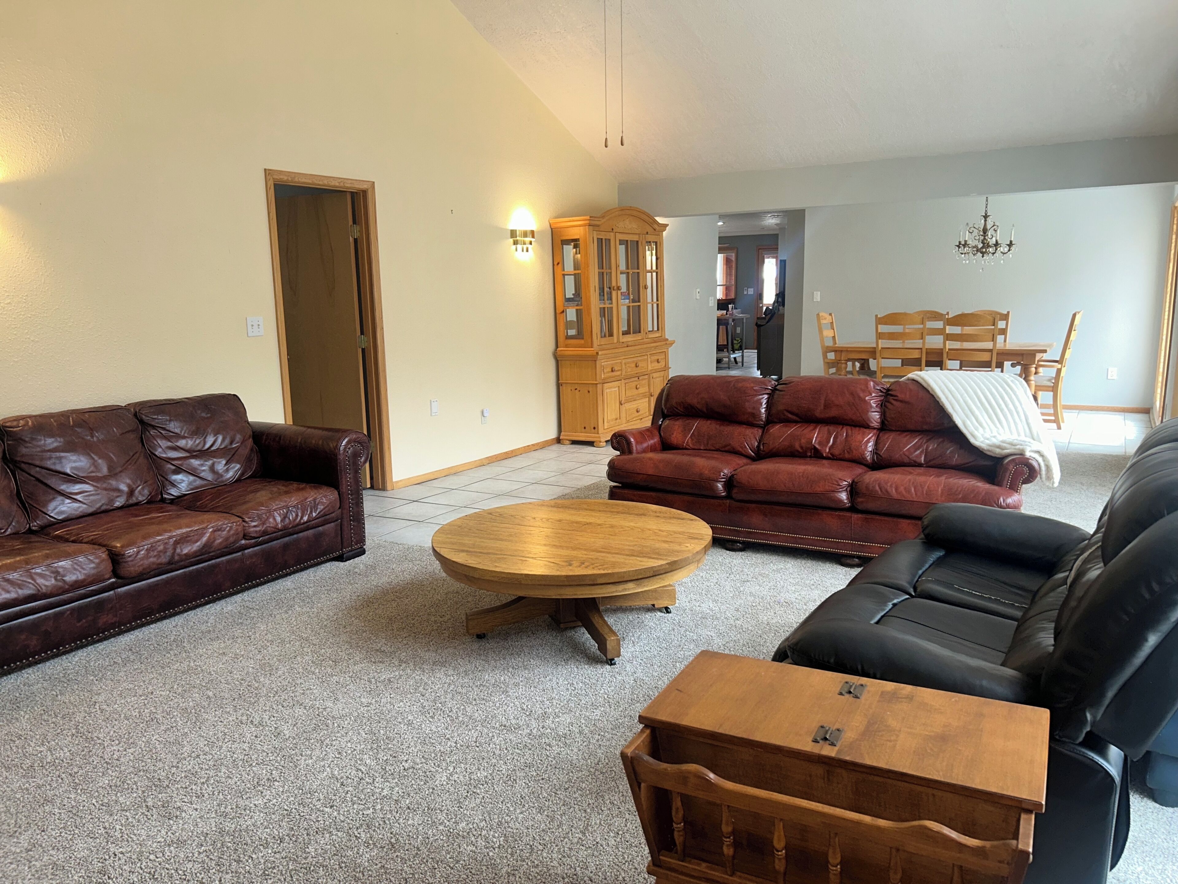A living room with a brown leather sofa, a red leather sofa, and a black leather sofa. There is a wooden coffee table in the center.
