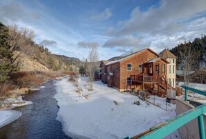 Une cabane en bois dotée d’un balcon, une rivière au premier plan et un paysage enneigé.