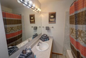 Une salle de bain avec un lavabo blanc, un miroir et un rideau de douche à motifs géométriques.