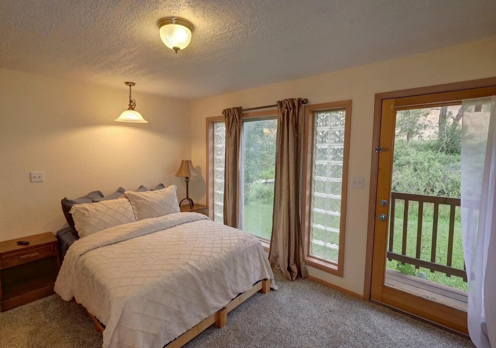 Ein Schlafzimmer mit einem Bett, einem Nachttisch, einer Lampe und Blick auf einen Garten durch eine Tür.