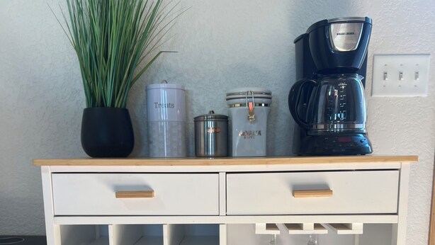 Un carrito de cocina blanco con cajones, estantes y una cafetera.