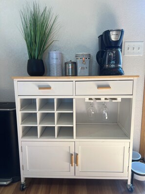 Un carrito de cocina blanco con cajones, estantes y una cafetera.