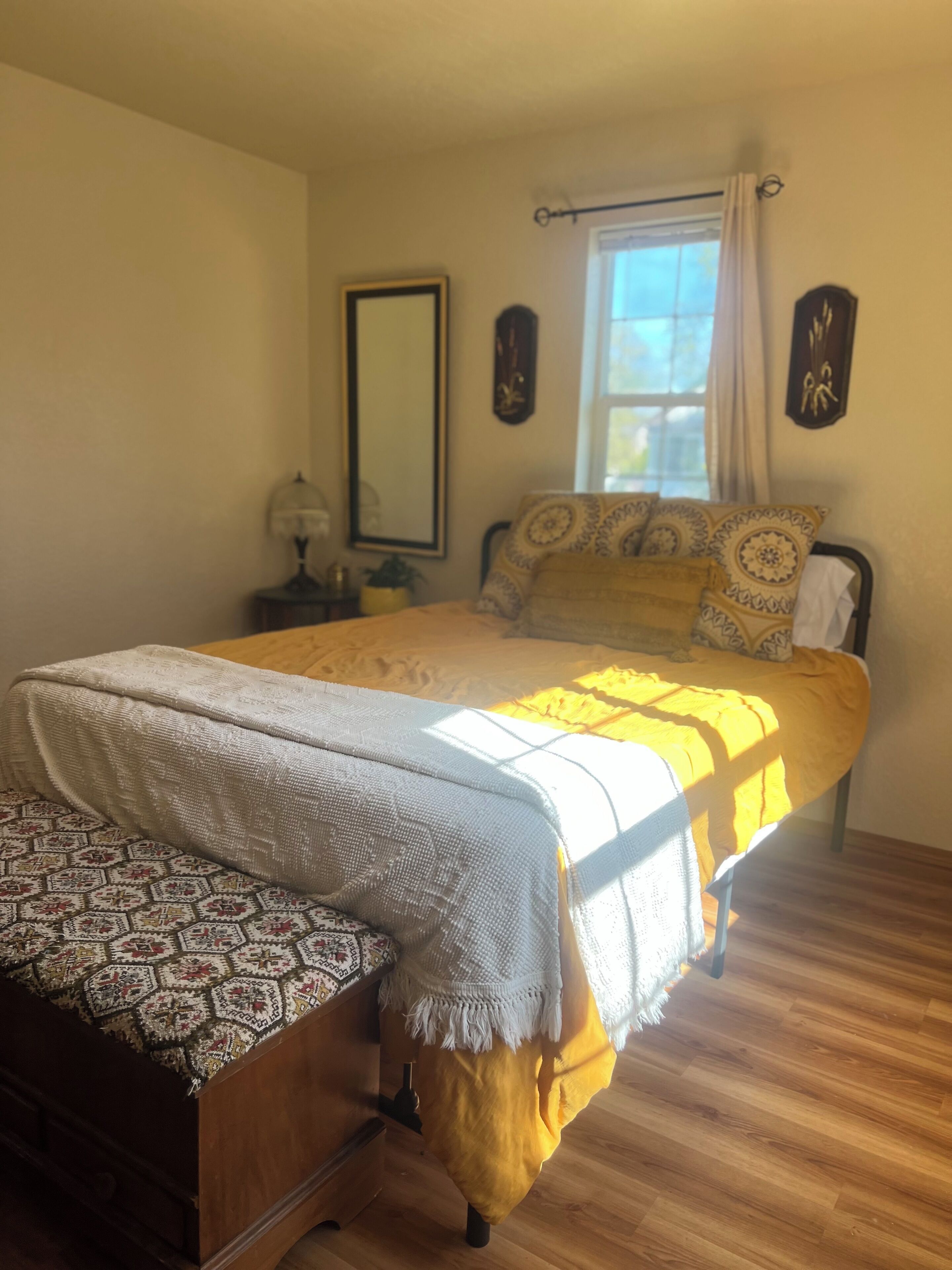 A bedroom with a bed, a bedside table, a mirror, and a window with curtains.