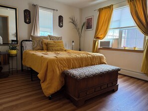 Un dormitorio con una cama, un banco de madera, un espejo y una ventana con cortinas.