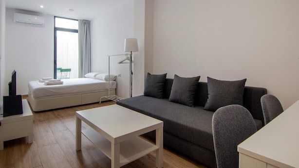 Een moderne, goed verlichte kamer met een bed, een grijze bank, een kleine tafel en een lamp.