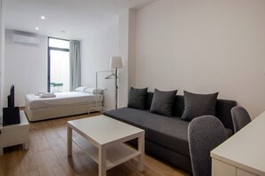 Una habitación moderna y luminosa con una cama, un sofá gris, una mesita y una lámpara.