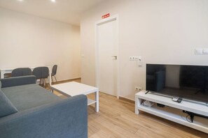 A modern living room with a grey sofa, a white coffee table, a flat-screen TV on a white stand, and a door with a sign.
