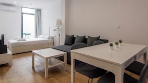 Een moderne, goed verlichte kamer met een bed, een bank, een eettafel en een klein keukentje.