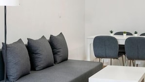 Een moderne woonkamer met een grijze bank, een witte salontafel en een eethoek met twee stoelen en een tafel.