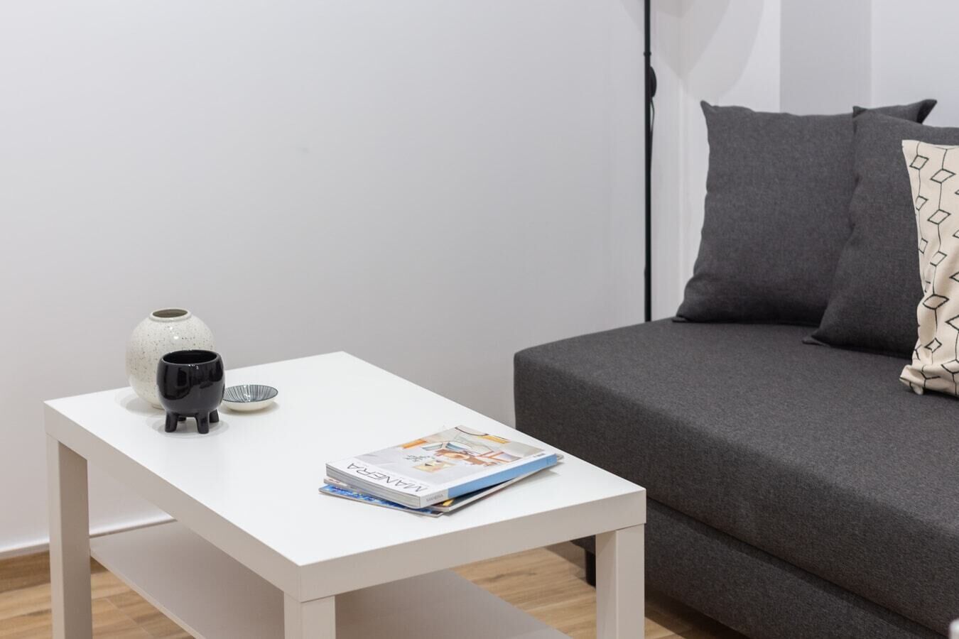 A small white table with a book, a black bowl, and a white vase.