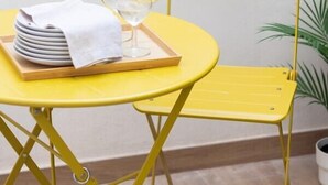 A yellow metal chair and table with a tray holding plates and a glass. - VLC HOST - Fray Pedro B (Valencia)