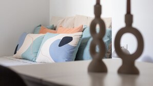 A neatly arranged bed with multiple pillows in various colors and patterns, a bedside table with a lamp, and a wall-mounted light fixture. - VLC HOST - Fray Pedro B (Valencia)