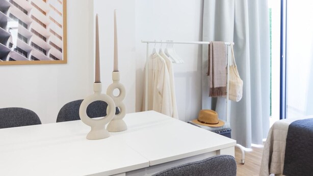 A modern hotel room with a white table, two candle holders, a clothing rack with a hat, and a window with curtains. - VLC HOST - Fray Pedro B (Valencia)