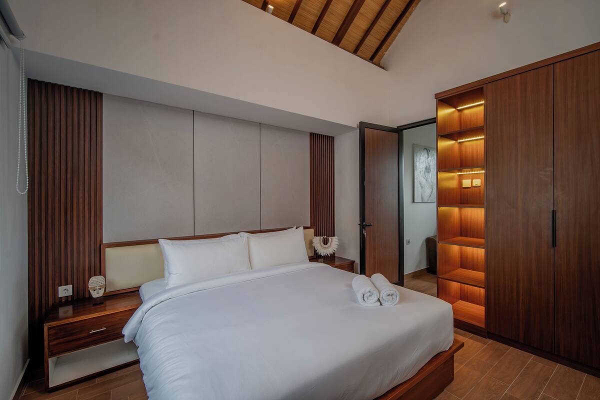 A modern hotel room with a large bed, wooden headboard, and built-in wardrobe.