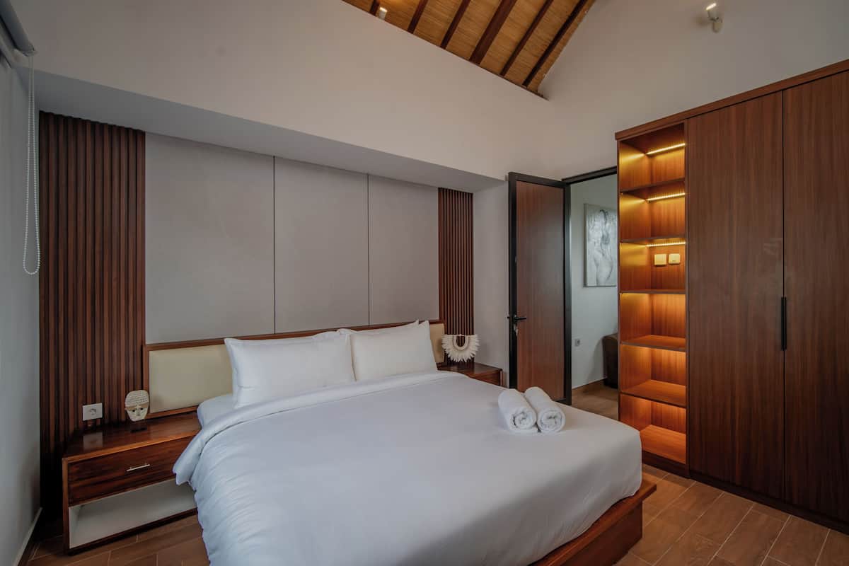 Ein modernes Hotelzimmer mit einem großen Bett, einem Holzkopfende und einem eingebauten Kleiderschrank.