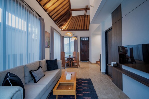 A modern living room with a sofa, coffee table, and dining area with chairs. - Avana Villa Jimbaran By Fays Hospitality (Jimbaran)