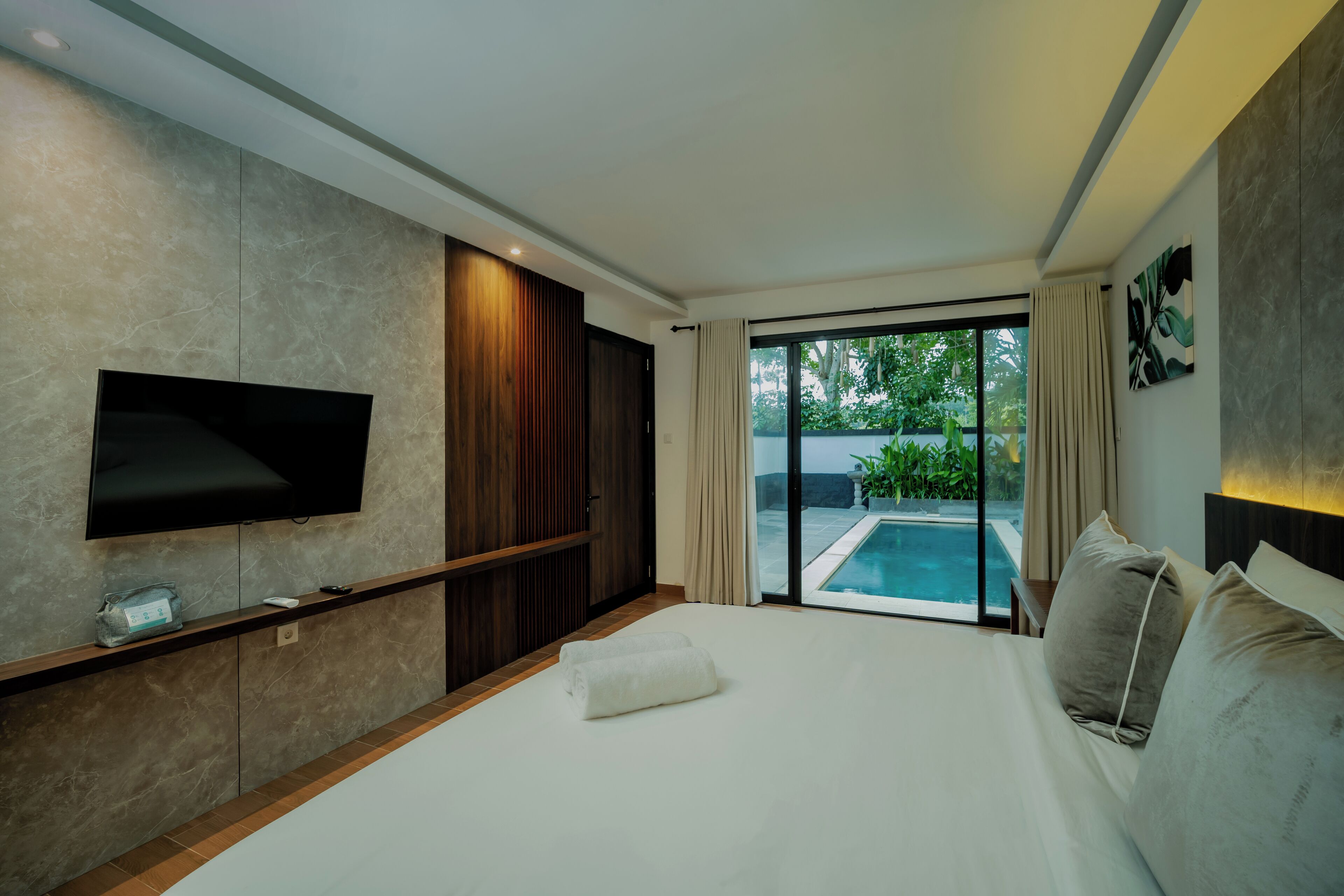 A modern hotel room with a large bed, a flat-screen TV mounted on the wall, and a view of a swimming pool through a sliding glass door.