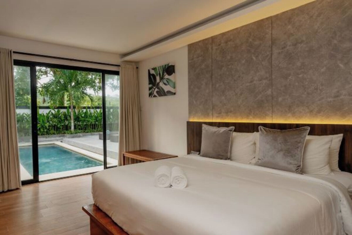 A hotel room with a large bed, a view of a swimming pool, and a wooden nightstand.