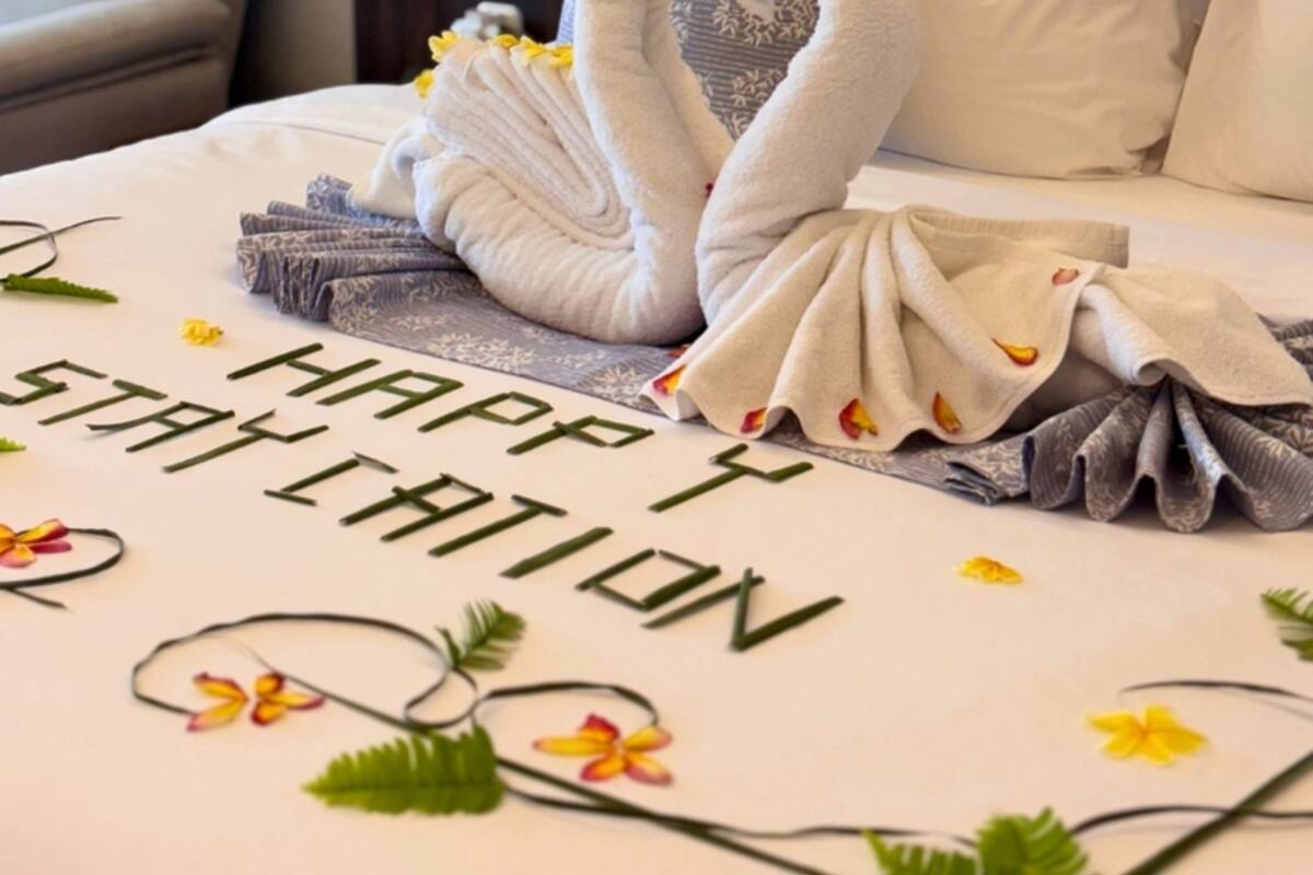 A bed with a decorative towel arrangement in the shape of swans, a message on the bedspread, and a headboard.