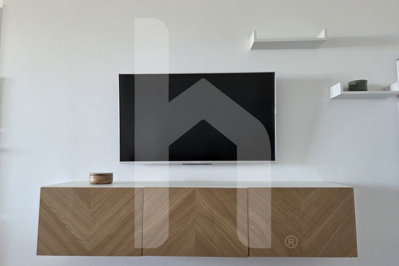 Un téléviseur à écran plat fixé au mur, au-dessus d’un meuble en bois orné d’un motif en chevrons.